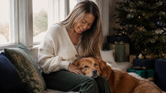Dog resting with its owner beside a Christmas tree and wrapped gifts
